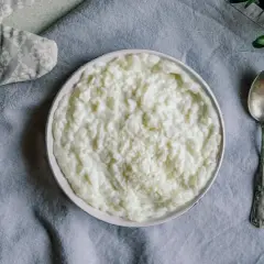 Miseczka z kleikiem ryżowym, obok łyżeczka i zielona gałązka.