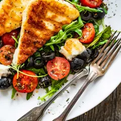 Pyszna sałatka z grillowanym halloumi, pomidorkami koktajlowymi i czarnymi oliwkami na talerzu.