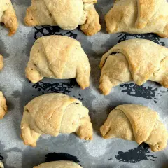 Upieczone rogaliki krucho drożdżowe, złociste i apetyczne, leżą na papierze do pieczenia.
