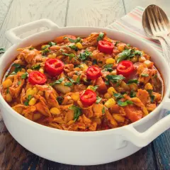 Aromaticzny gulasz z kurczaka z kukurydzą i papryczką chili, posypany świeżą natką pietruszki, podany w białej misie.