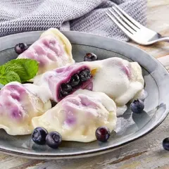 Pyszne pierogi z jagodami, polane śmietaną, ozdobione miętą i świeżymi owocami. Idealne na deser.
