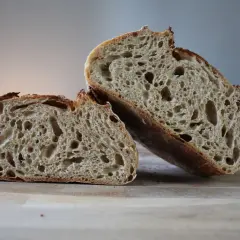 Chleb pszenno żytni na zakwasie, przekrojony na pół, ukazuje puszysty miąższ z licznymi dziurami i chrupiącą skórkę.