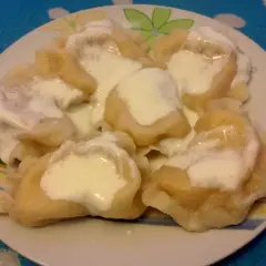 Talerz pełen pysznych pierogów ruskich, polanych śmietaną. Idealne na obiad, zgodnie z tradycyjnym pierogi ruskie przepis.