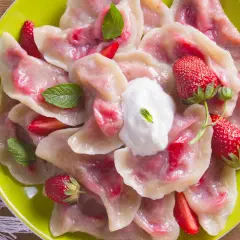 Pyszne pierogi z truskawkami, udekorowane miętą i śmietaną, na zielonym talerzu.