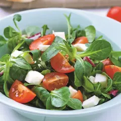 Świeża sałatka z roszponką, pomidorkami koktajlowymi i kostkami sera mozzarella w pastelowej misce.