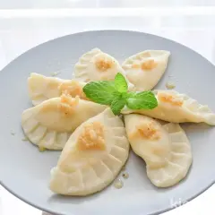 Pyszne pierogi z serem, udekorowane miętą i posypką, ułożone na talerzu w kształt kwiatu.