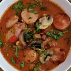 Gęste leczo z pieczarkami, kiełbasą i warzywami, posypane natką pietruszki, w białej misce.