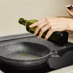Oliwa z oliwek leje się z butelki do patelni. Tak, na oliwie z oliwek można smażyć.