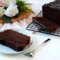 Wilgotna babka czekoladowa z polewą, podana na talerzyku z widelcem. Obok leży reszta ciasta na kratce.