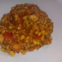 Pyszne kaszotto z kurczakiem, kukurydzą i pomidorami na białym talerzu.