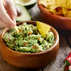 Ręka zanurza chipsa w misce z guacamole. To pyszne, zielone danie, idealne do nachosów.