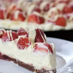 Pyszna tarta z truskawkami, udekorowana kremem i białym lukrem. Kawałek na talerzyku kusi świeżością i słodyczą.