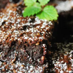 Wilgotny brownie z malinami, posypany cukrem pudrem i udekorowany listkiem mięty. Idealny deser na każdą okazję.