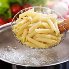 Gotujesz makaron penne, pierwszy krok, jak zrobić spaghetti. W tle pomidory i sałata.