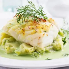 Pyszna ryba w sosie koperkowym, podana na purée ziemniaczanym z dodatkiem świeżego koperku. Danie wygląda apetycznie i aromatycznie.