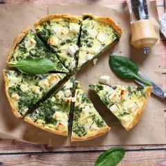 Pyszna tarta ze szpinakiem i fetą, pokrojona na kawałki, z listkami świeżego szpinaku i pieprzniczką w tle.