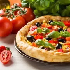 Pyszna pizza z pomidorami, oliwkami i kukurydzą, obok świeże pomidory i bazylia. Idealna na letni obiad.