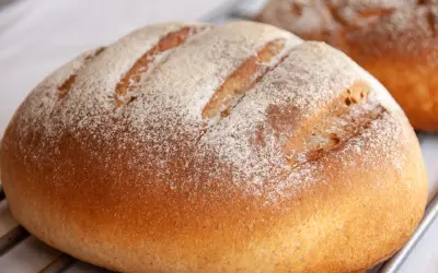 Chleb na maślance, lekko oprószony mąką, z widocznymi nacięciami na skórce. Pachnie świeżością i domowym ciepłem.
