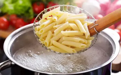 Gotujesz makaron penne, pierwszy krok, jak zrobić spaghetti. W tle pomidory i sałata.