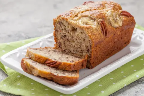 Pyszny chlebek bananowy fit z orzechami pekan i plasterkami banana na wierzchu, pokrojony na kromki.