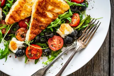 Pyszna sałatka z grillowanym halloumi, pomidorkami koktajlowymi i czarnymi oliwkami na talerzu.
