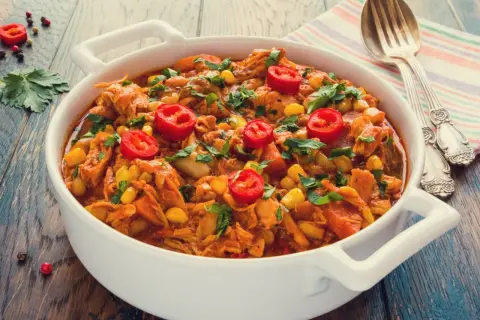 Aromaticzny gulasz z kurczaka z kukurydzą i papryczką chili, posypany świeżą natką pietruszki, podany w białej misie.