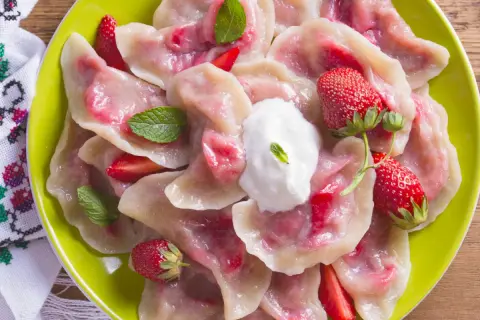 Pyszne pierogi z truskawkami, udekorowane miętą i śmietaną, na zielonym talerzu.