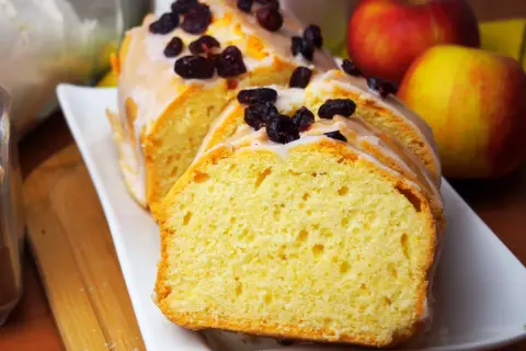 Szybka babka wilgotna, polana lukrem i posypana żurawiną, obok jabłek. Idealna na deser.