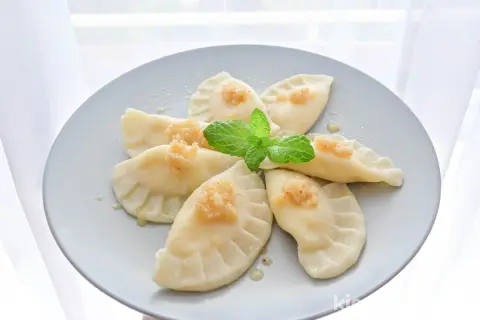 Pyszne pierogi z serem, udekorowane miętą i posypką, ułożone na talerzu w kształt kwiatu.