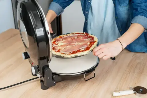 Osoba wkłada pizzę do pieca. Zastanawiasz się, w jakiej temperaturze piec pizzę? Ten piec jest idealny do domowych wypieków.
