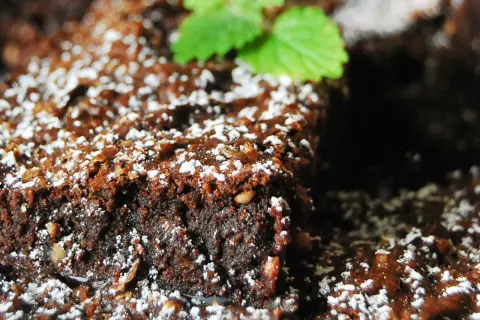 Wilgotny brownie z malinami, posypany cukrem pudrem i udekorowany listkiem mięty. Idealny deser na każdą okazję.