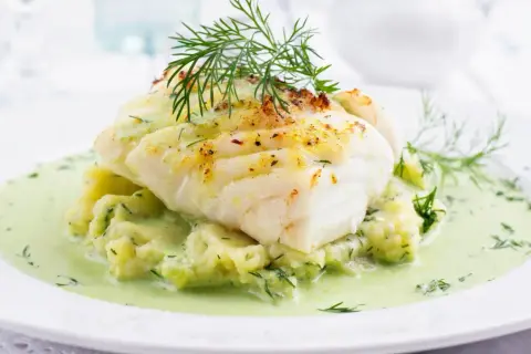 Pyszna ryba w sosie koperkowym, podana na purée ziemniaczanym z dodatkiem świeżego koperku. Danie wygląda apetycznie i aromatycznie.