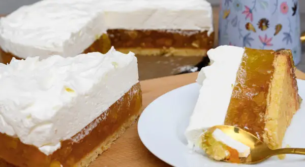 Pyszny tort z warstwą owocową i puszystym kremem śmietankowym do tortu. Na talerzyku kawałek z widelcem.