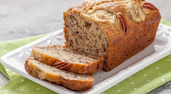 Pyszny chlebek bananowy fit z orzechami pekan i plasterkami banana na wierzchu, pokrojony na kromki.