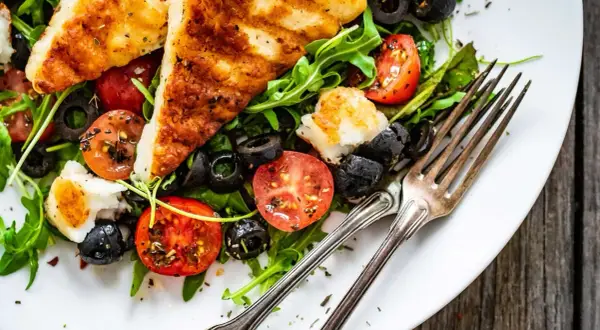 Pyszna sałatka z grillowanym halloumi, pomidorkami koktajlowymi i czarnymi oliwkami na talerzu.