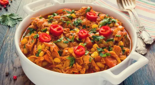 Aromaticzny gulasz z kurczaka z kukurydzą i papryczką chili, posypany świeżą natką pietruszki, podany w białej misie.
