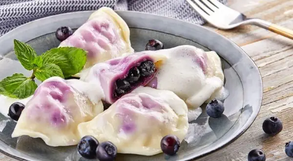 Pyszne pierogi z jagodami, polane śmietaną, ozdobione miętą i świeżymi owocami. Idealne na deser.