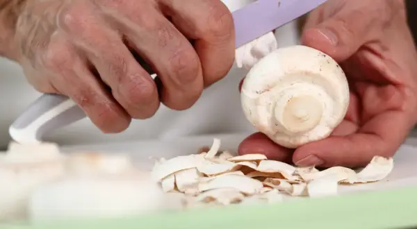 Ręce obierają pieczarkę, usuwając skórkę. Czy pieczarki trzeba obierać? Zależy od preferencji, ale często się je obiera.
