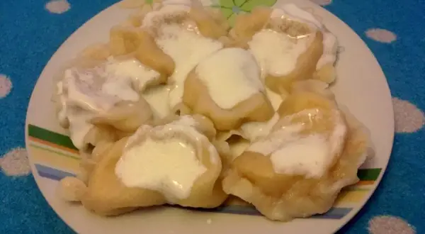 Talerz pełen pysznych pierogów ruskich, polanych śmietaną. Idealne na obiad, zgodnie z tradycyjnym pierogi ruskie przepis.