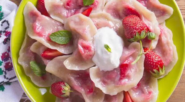 Pyszne pierogi z truskawkami, udekorowane miętą i śmietaną, na zielonym talerzu.