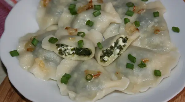Pyszne pierogi ze szpinakiem i serem, posypane szczypiorkiem i skwarkami. Idealne na obiad!