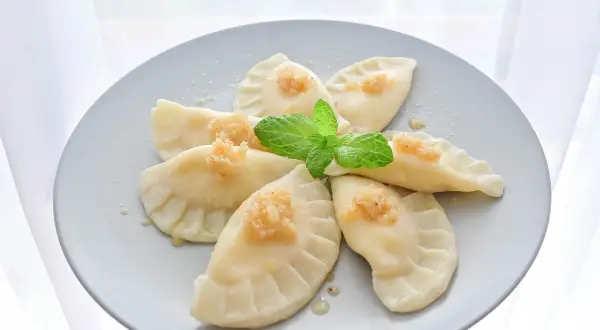 Pyszne pierogi z serem, udekorowane miętą i posypką, ułożone na talerzu w kształt kwiatu.