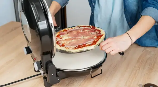 Osoba wkłada pizzę do pieca. Zastanawiasz się, w jakiej temperaturze piec pizzę? Ten piec jest idealny do domowych wypieków.