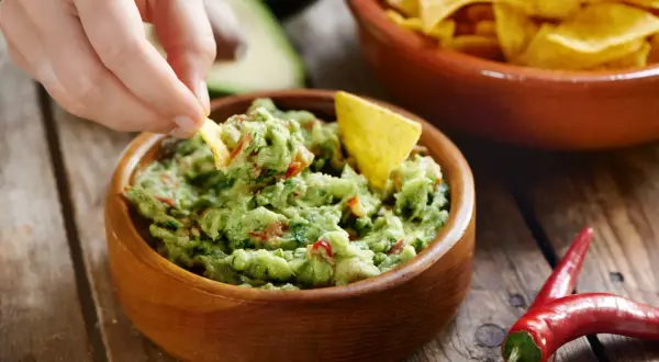 Ręka zanurza chipsa w misce z guacamole. To pyszne, zielone danie, idealne do nachosów.
