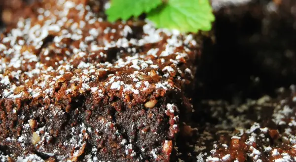 Wilgotny brownie z malinami, posypany cukrem pudrem i udekorowany listkiem mięty. Idealny deser na każdą okazję.
