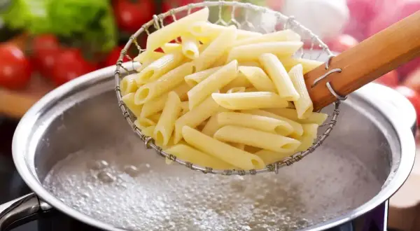 Gotujesz makaron penne, pierwszy krok, jak zrobić spaghetti. W tle pomidory i sałata.
