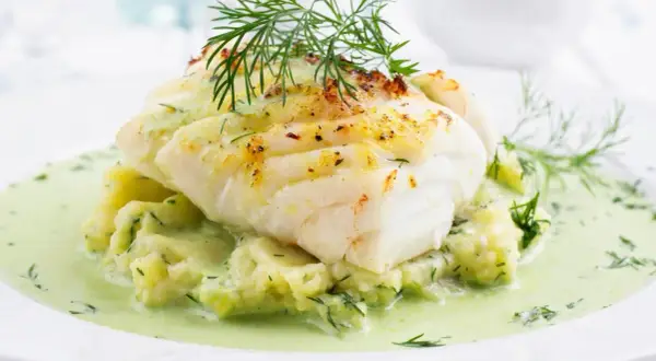 Pyszna ryba w sosie koperkowym, podana na purée ziemniaczanym z dodatkiem świeżego koperku. Danie wygląda apetycznie i aromatycznie.