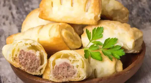 Stos pieczonego ciasta francuskiego z kiełbasą w środku, ozdobione natką pietruszki.