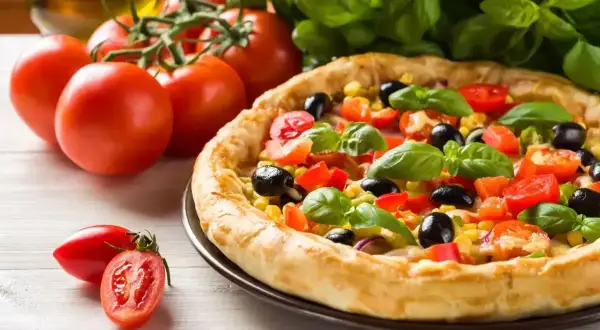 Pyszna pizza z pomidorami, oliwkami i kukurydzą, obok świeże pomidory i bazylia. Idealna na letni obiad.