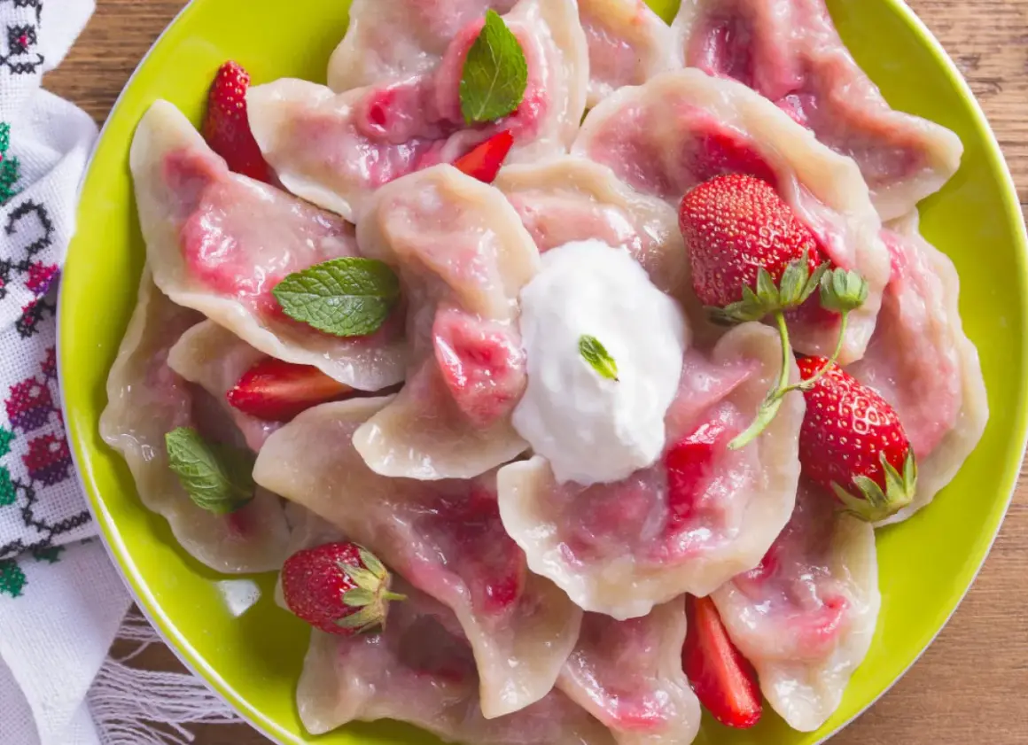 Pyszne pierogi z truskawkami, udekorowane miętą i śmietaną, na zielonym talerzu.
